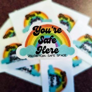 A group of stickers. they feature a rainbow and the words "You're Safe Here 2SLGBTQIA+ Safe Space"